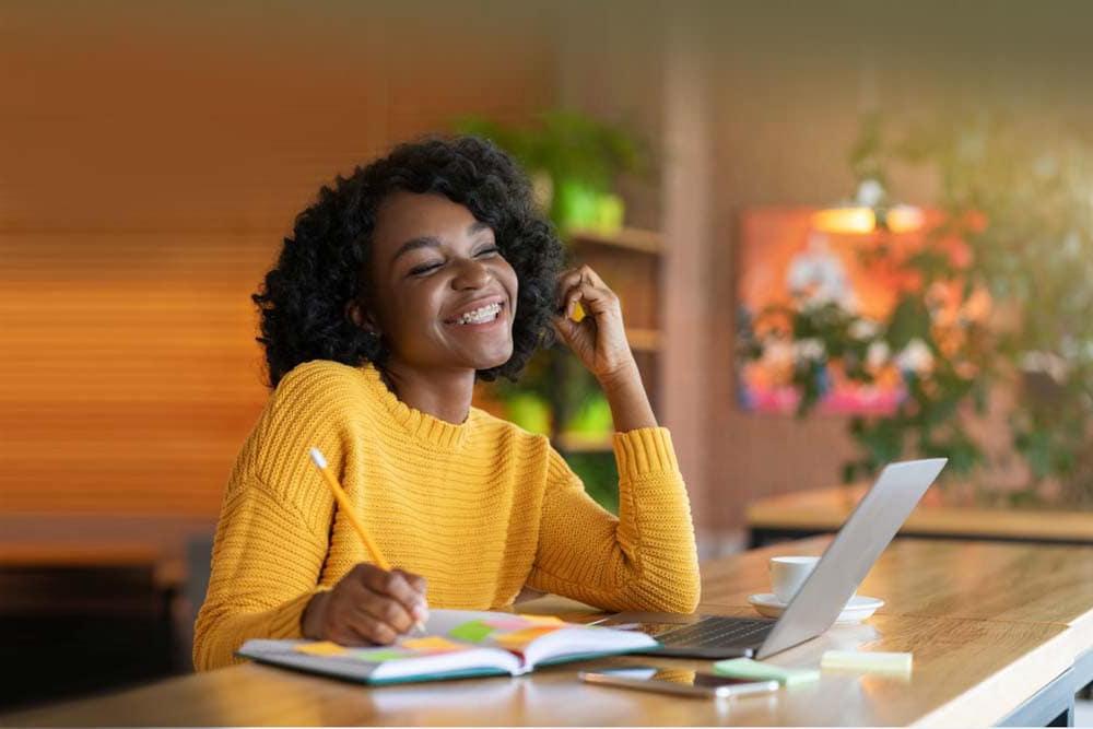 Young girl in a yellow sweater writing in a notebook while watching a lesson on a computer taking an online class at Virginia Connections Academy. 