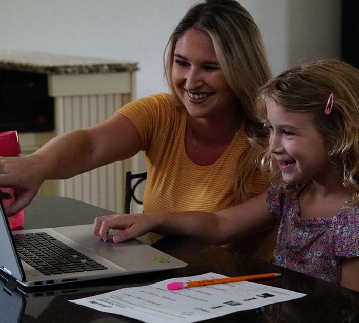 A mother and her dauther pointing at the laptop screen during an online lesson