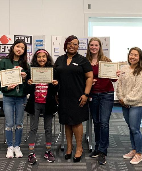 A teacher standing next to her students who are holding certificates